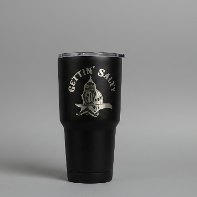A matte black insulated travel tumbler with a clear lid, featuring a silver engraved graphic and the words 'GETTIN' SALTY' on the front, displayed on a white rectangular box against a gray studio background.