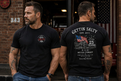 Man standing outdoors in front of a brick building doorway, wearing black graphic T-shirts. The man on the left shows the front chest logo, and the man on the right shows the back with a large white memorial-style graphic reading 'Gettin' Salty', 'Est.