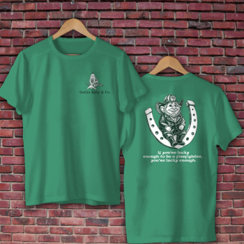Two green t-shirts with graphic designs on hangers against a brick wall background.