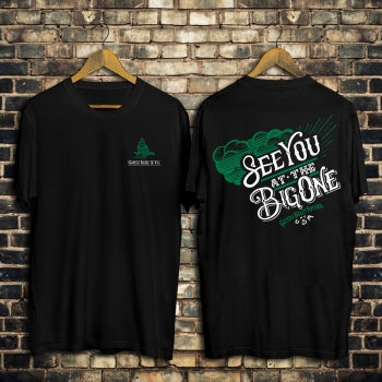 Two black t-shirts hanging on a brick wall, one with a logo and the other with text.