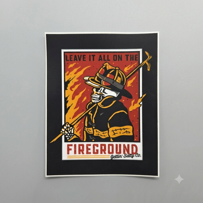 A framed art print featuring a stylized firefighter skeleton holding a hose, with flames in the background and the text 'LEAVE IT ALL ON THE FIREGROUND Gettin' Sandy Co.' on a light gray wall.